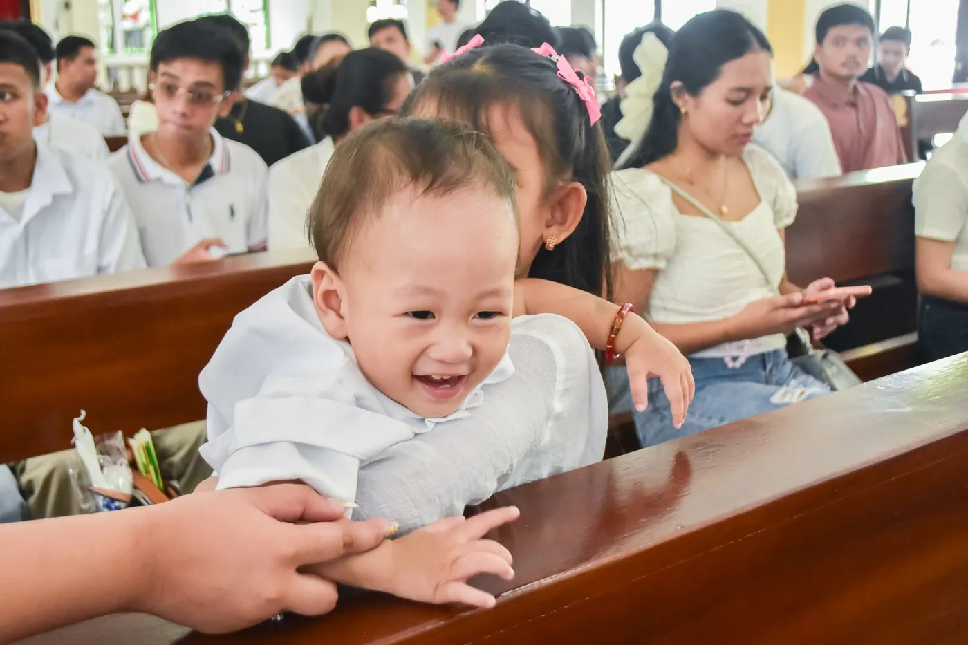 Baby in a white outfit smiling over a church pew during a baptism