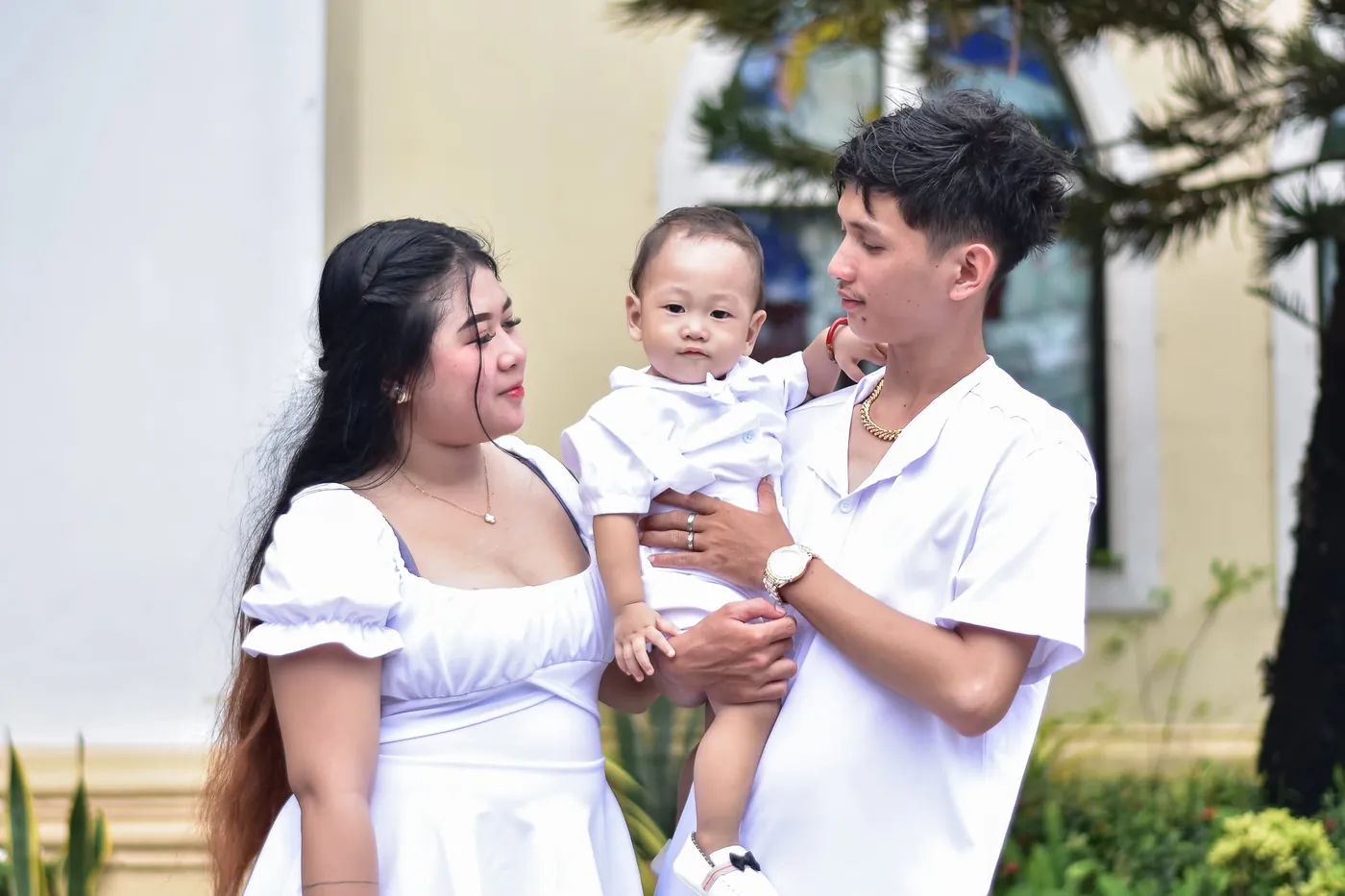 Parents in white holding their baby on the church grounds after a baptism