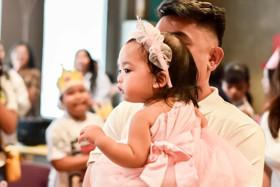Toddler in a pink tutu dress held in her dad's arms, warm natural light