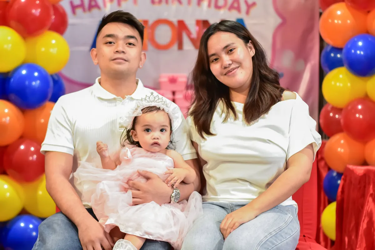 Family portrait of a couple with their baby on a red couch in front of a balloon backdrop
