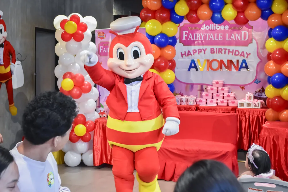 Mascot beside a birthday cake and decorated backdrop with balloons at an event in Cavite