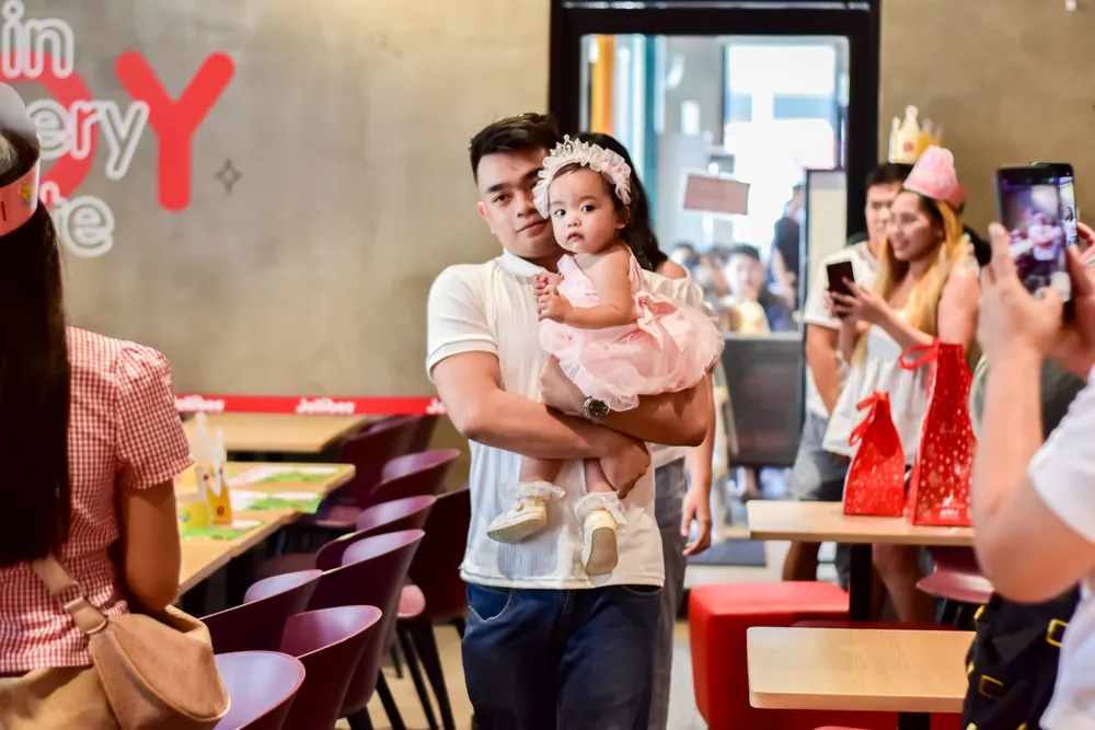 Dad carrying his daughter through a busy party venue while guests take photos