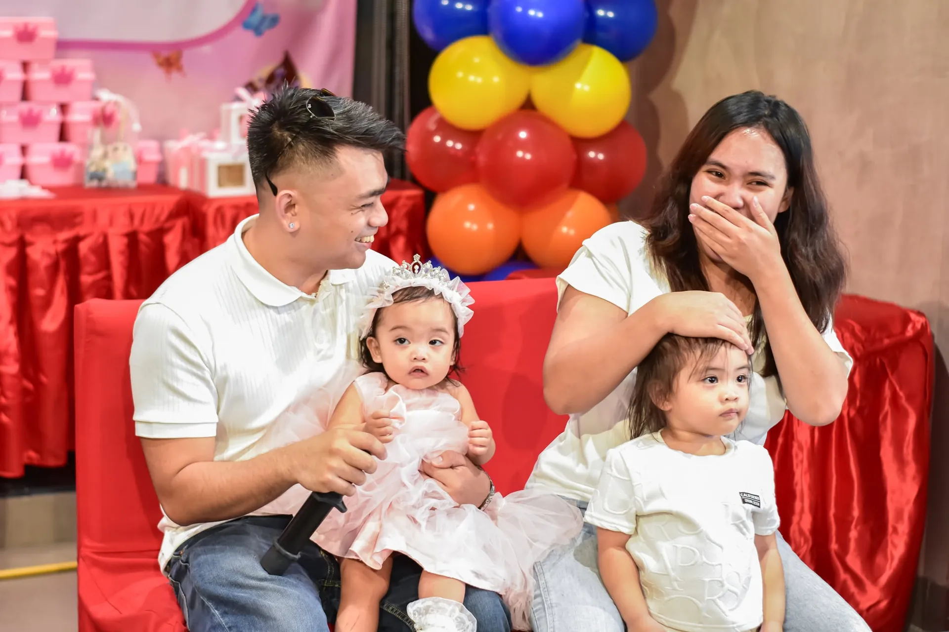 Parents laughing with their two little girls on a red couch at a birthday party in Imus, Cavite, photographed by Dana Shotz