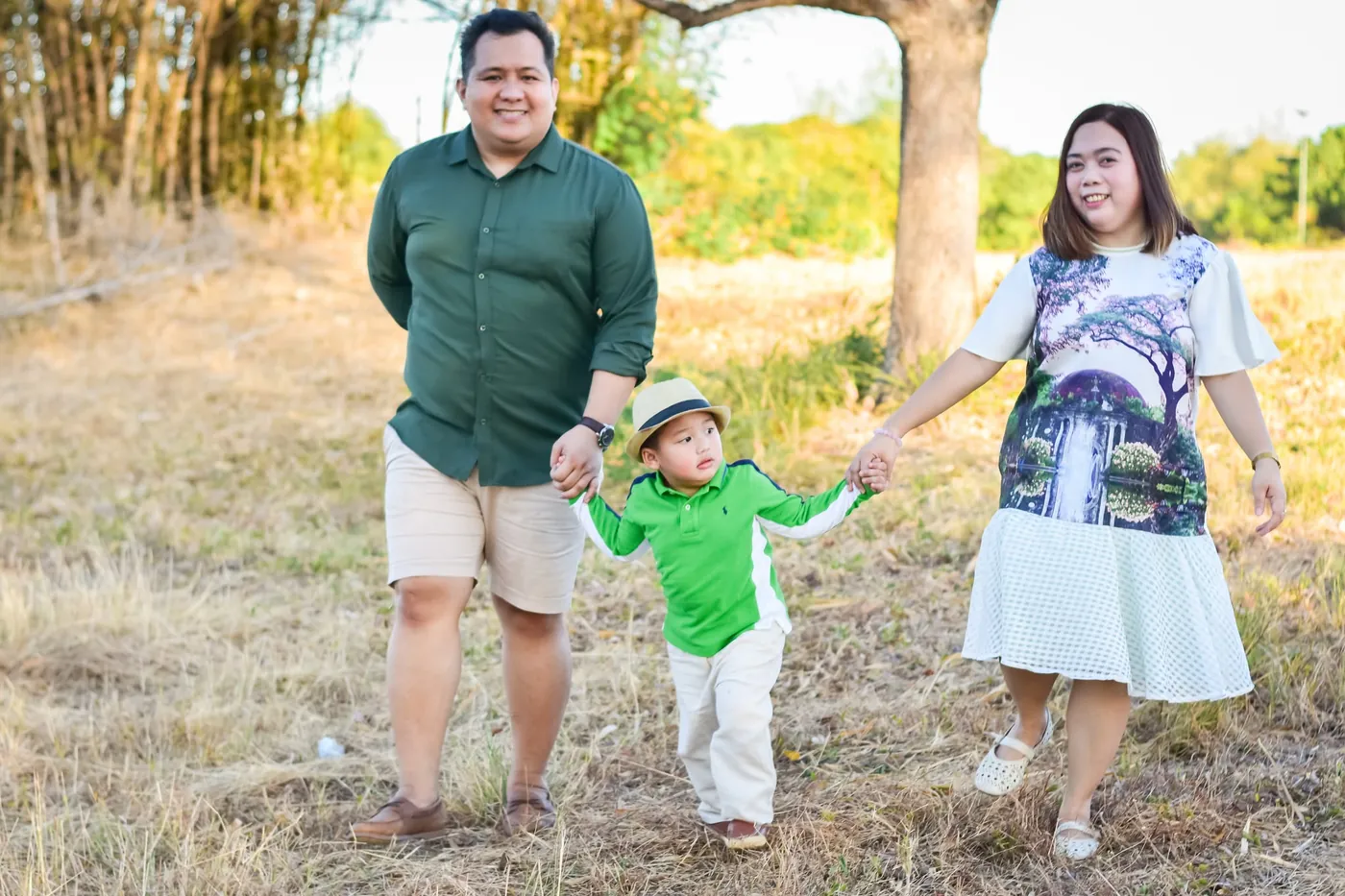 Parents walking hand in hand with their toddler across a grassy field during an outdoor family photoshoot