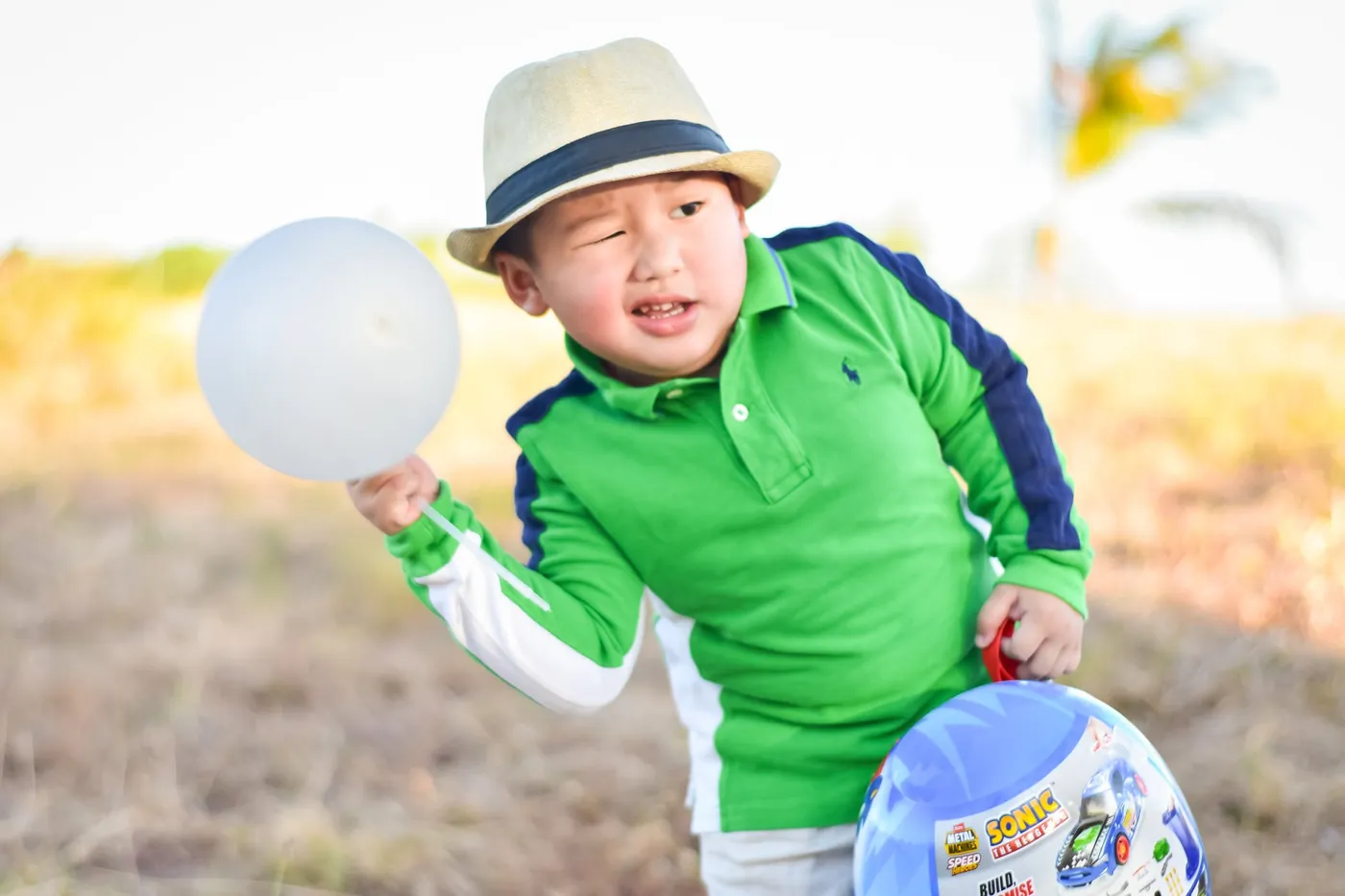 Toddler squinting and laughing while holding a balloon in warm backlight